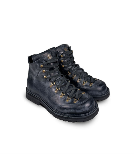 Close-up 3/4 view of the Untitled Artworks x Fracap Destroyer Boot in black, showcasing its spray-effect finish, oversized fold-over tongue, and antique brass eyelets.