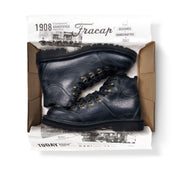 Close-up in box view of the Untitled Artworks x Fracap Destroyer Boot in black, showcasing its spray-effect finish, oversized fold-over tongue, and antique brass eyelets.